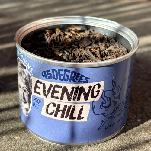 Close-up of an open round tea tin with a blue label that reads '95 Degrees EVENING CHILL'. The tin is filled with a premium loose leaf tea lapsang souchong blend.