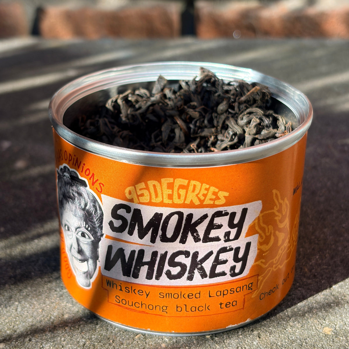 Close-up of an open orange tin can filled with coarse, loose-leaf 95degrees rocks Smokey Whiskey black tea